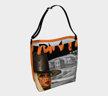 Load image into Gallery viewer, A tote bag with a black shoulder strap, featuring a graphic collage print of a woman in a black hat smoking a cigar, gray buildings, and bold orange lettering on a black background, set against a light gray studio backdrop.