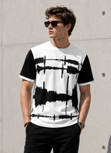 Load image into Gallery viewer, A man wearing a black and white color-blocked t-shirt with a black soundwave graphic across the front, styled with black pants, sunglasses, and a necklace, standing against a concrete wall.